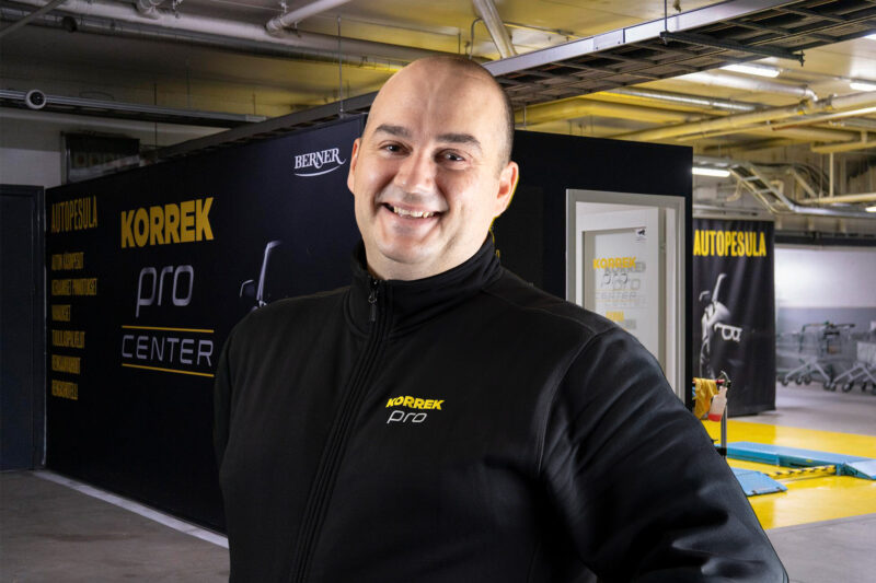 Hymyilevä Korrek Pro Center -yrittäjä poseeraa autopesulan edessä yllään musta Korrek Pro -logolla varustettu takki.