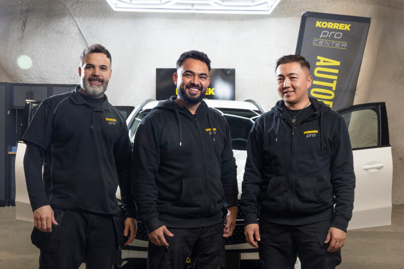 Kolme Korrek Pro Center -ammattilaista valkoisen auton edessä Korrek Pro Center -autopesussa.
